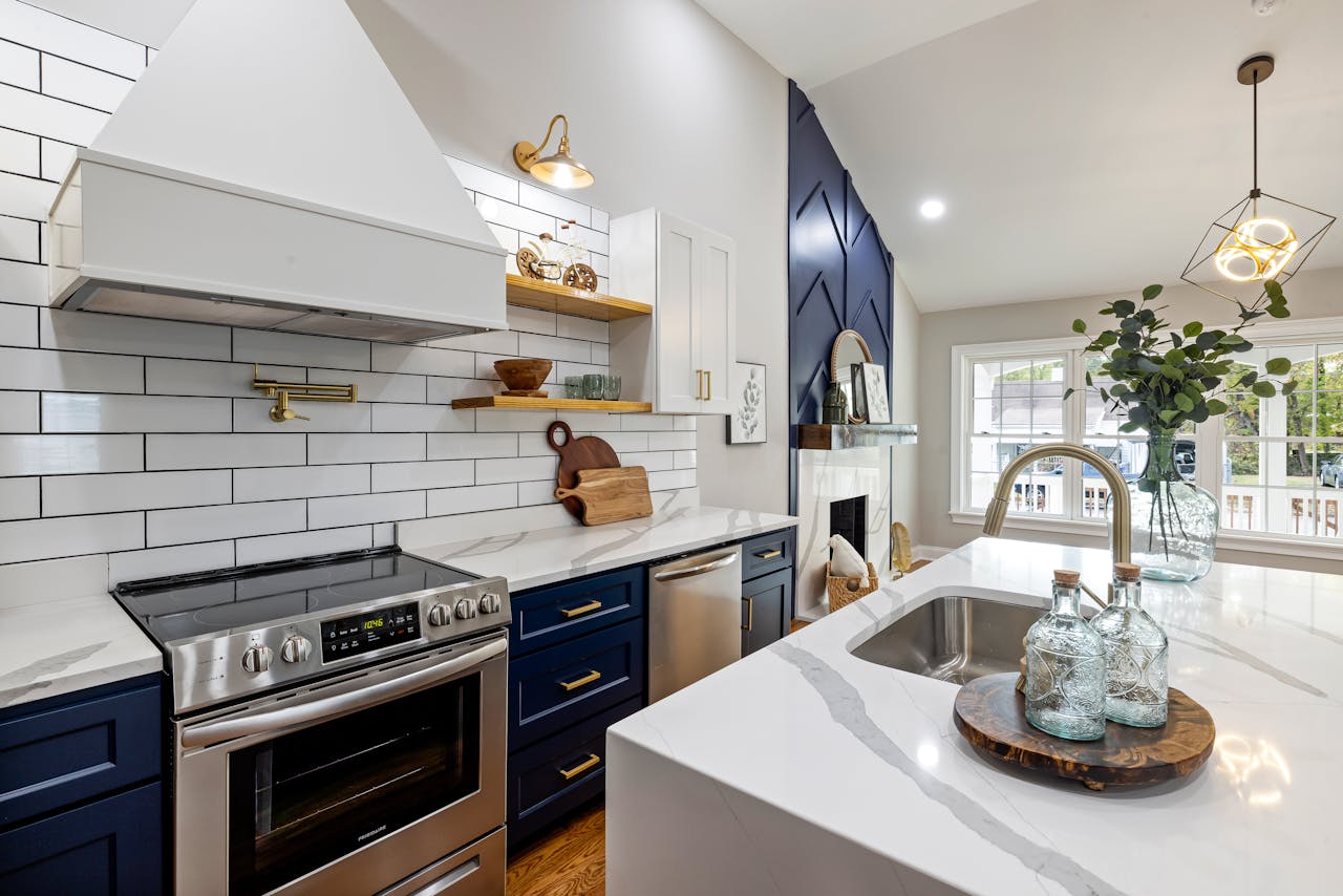 services-01 A modern kitchen featuring marble countertops, a stainless steel stove, and elegant blue cabinets.